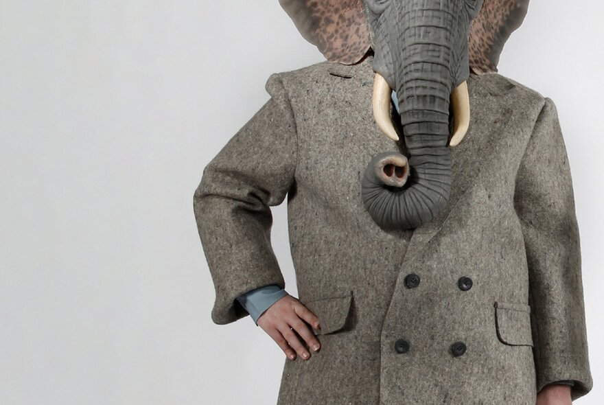 Mid-face downwards view of a creature in a grey overcoat with an elephant's head. 