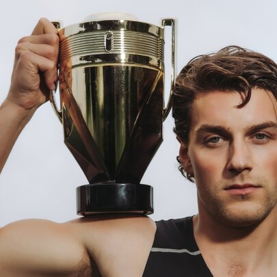 Man with coiffed hair and makeup holding gold sporting cup.