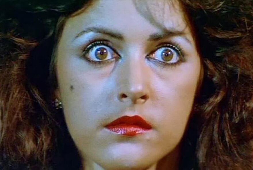 A still from an Indonesian horror film showing the face of a terrified young woman with eyes wide in horror.