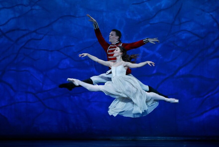 Two ballet dancers leaping in the air spectacularly in a production of The Nutcracker. 