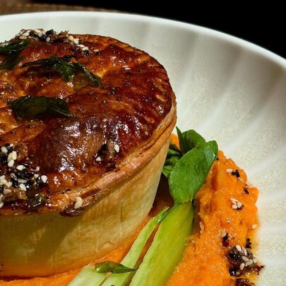 Close up of a crispy pie with a side of green vegetables on a white plate.