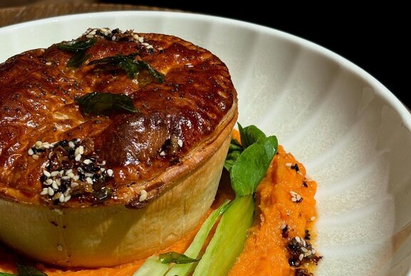 Close up of a crispy pie with a side of green vegetables on a white plate.