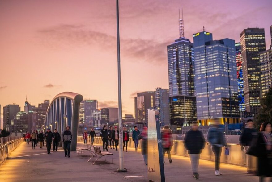 People walking across a city bridge at sunset in footy colours.