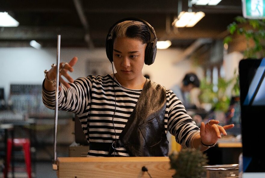 Person wearing headphones and striped shirt playing with electronic equipment.