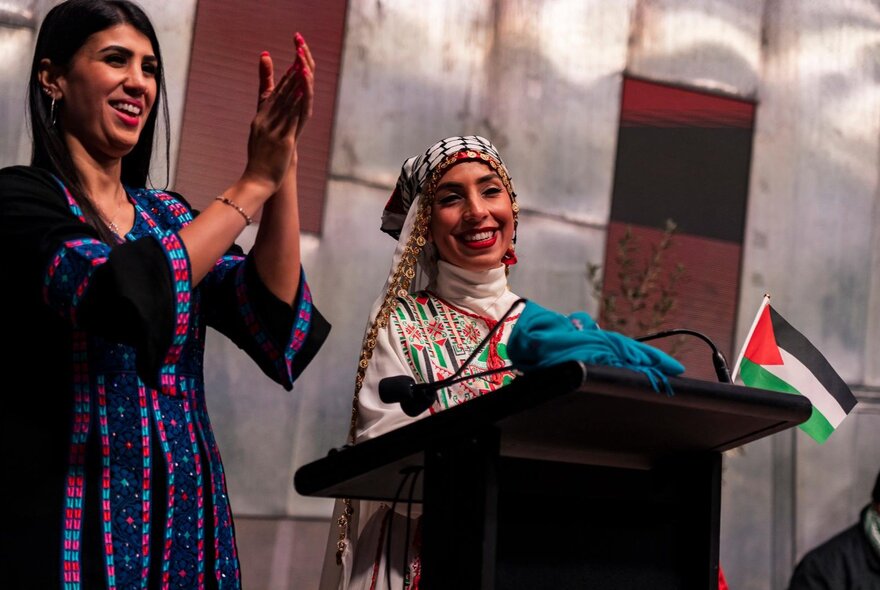 Two Palestinian woman standing at a podium at Fed Square in traditional clothing.