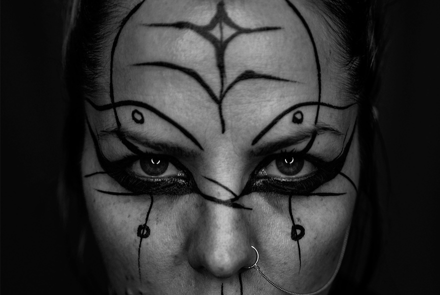 A monochrome close-up of a woman's face with lines and symbols drawn over her skin. 