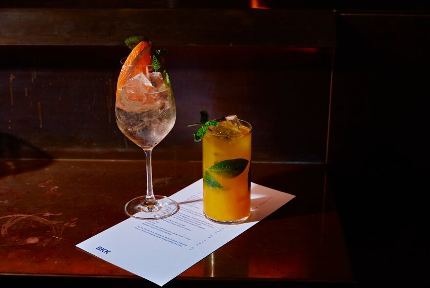 Two fruity cocktails resting on a drinks menu on a brown table.