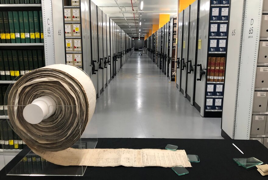 A roll of parchment with writing on it, displayed on a black table in the National Archives.