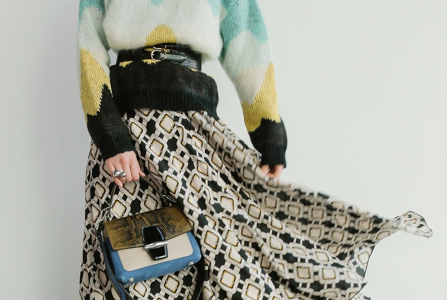 Woman in jumper and skirt and holding a handbag.