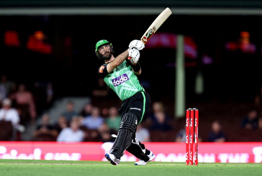 A batsman from the BBL Melbourne Stars after hitting a shot,  on green grass in front of red wickets.