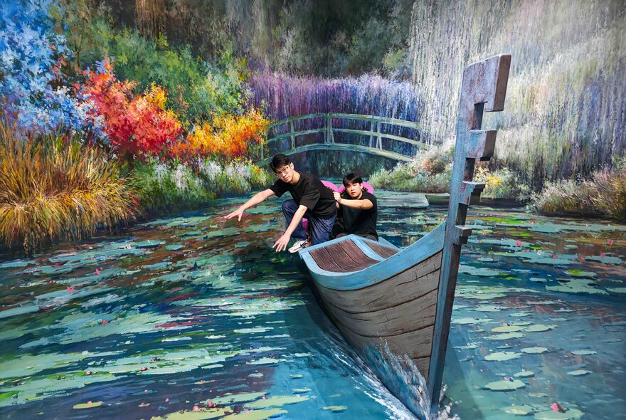 Two friends in exaggerated poses against a hand-painted interactive artwork of a boat in a river at ArtVo.