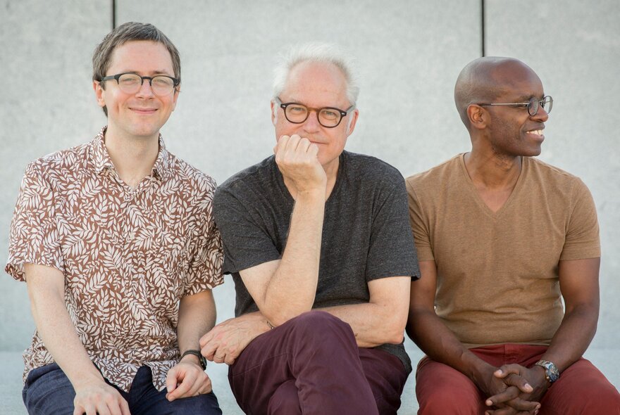 Seated older musical trio, all wearing glasses.