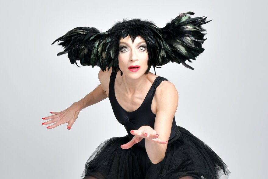 Performer dressed in a black tutu with winged hair, arms outstretched like a cat.