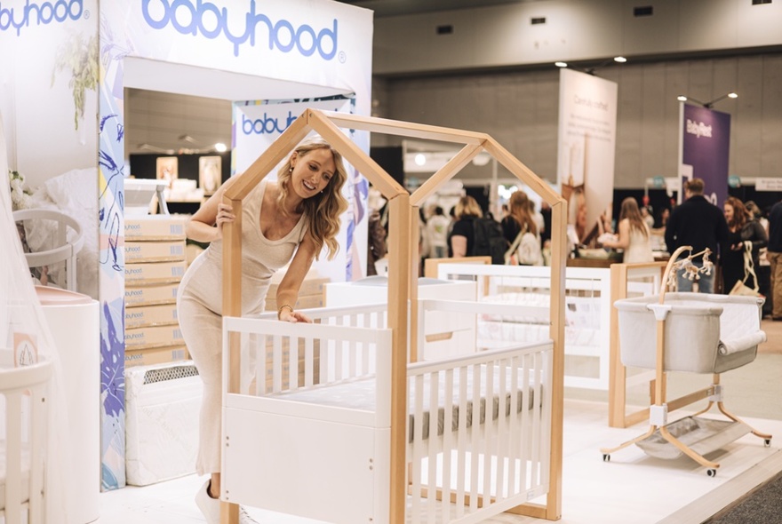 A pregnant woman looking into a crib at an expo baby products stand.