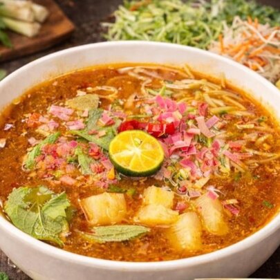 A bowl of vegan assam laksa with noodles, tofu and fresh herbs, garnished with a lime round in the centre.