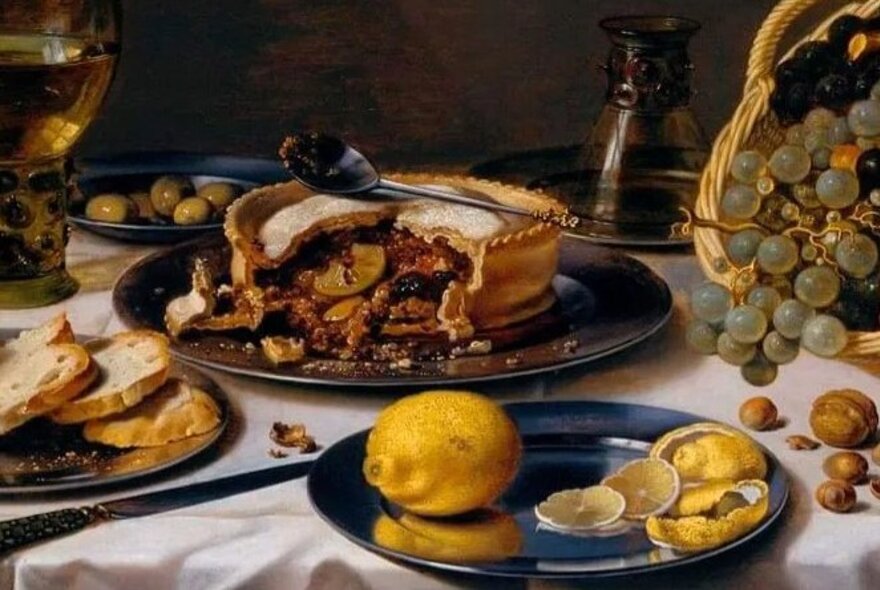 A still-life painting of a steak and kidney pie, grapes, slices of bread and lemons.