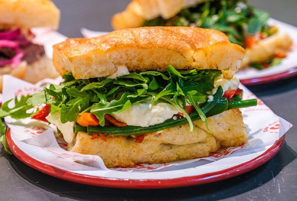 A focaccia sandwich with cheese, rocket and peppers in it.