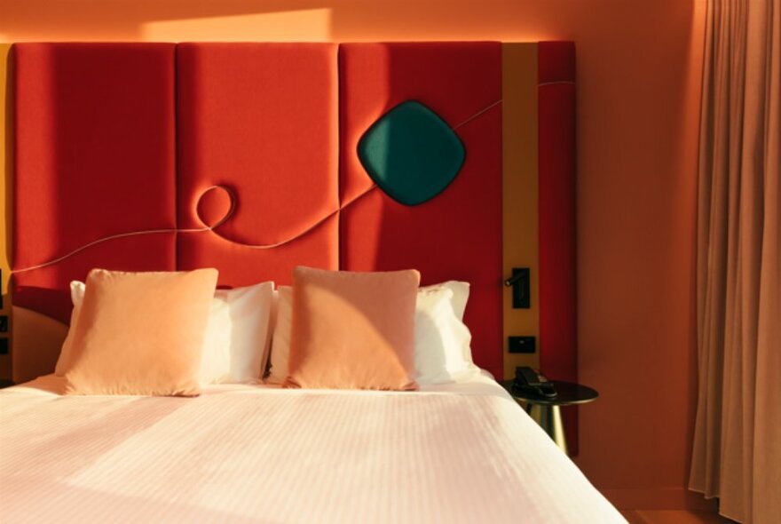 A queen size bed at Quincy Hotel Melbourne with a red padded headboard and peach coloured walls.