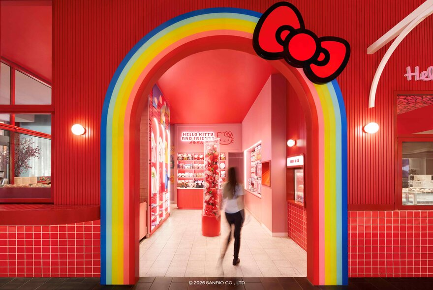 The rainbow entrance to a red shopfront; a woman walking into the store.