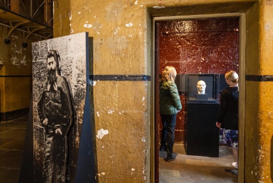 An exhibit in the Old Melbourne Gaol with an old photo of Ned Kelly and a doorway leading through to another room. 