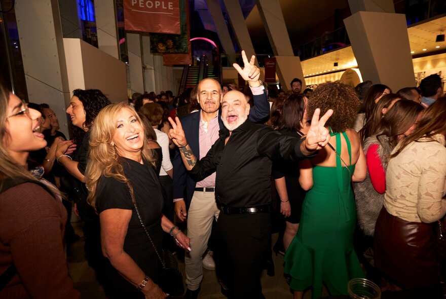 A lively indoor gathering at Melbourne Museum, with several people smiling and making peace signs while dancing or posing for a photo.