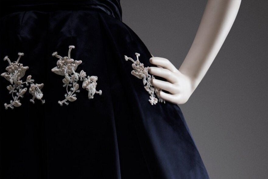 A mannequin's hand resting on a blue velvet gown with elaborate silver diamante detailing.