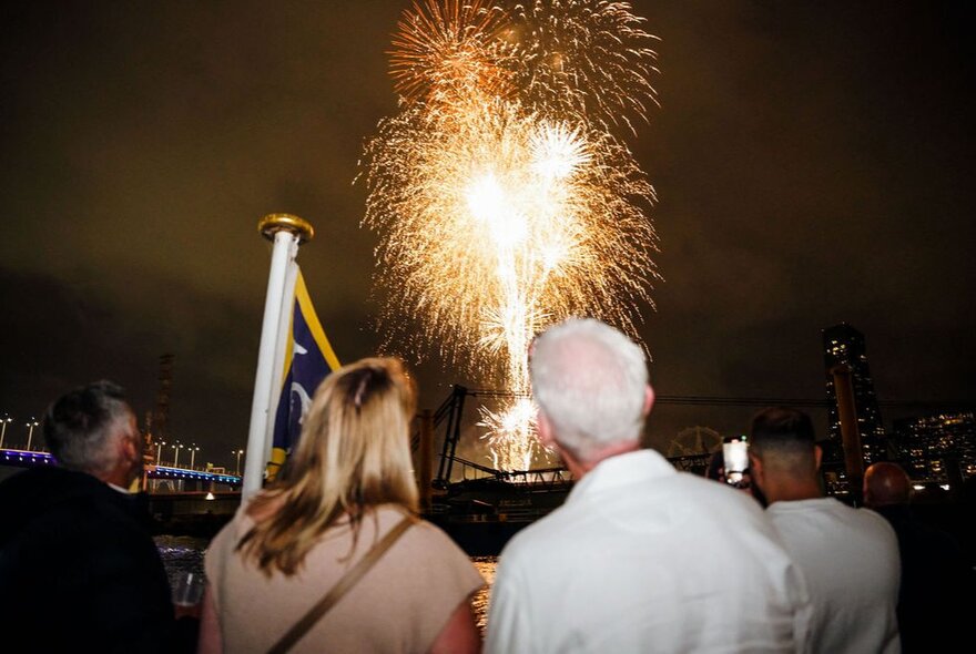 People watching a fireworks display over the City of Melbourne from a boat on the Yarra River. 