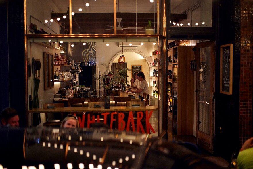 Interior of a small neighbourhood wine bar from the street, looking through large glass windows.