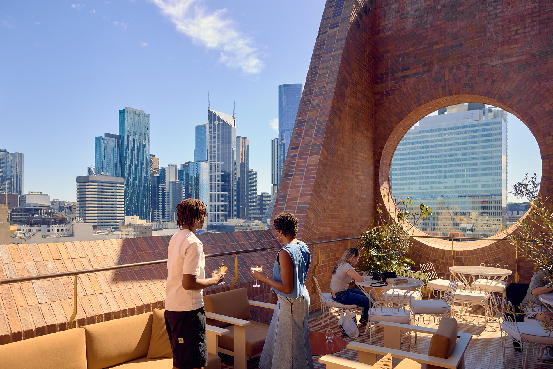Two friends drinking on a city rooftop on a sunny day.
