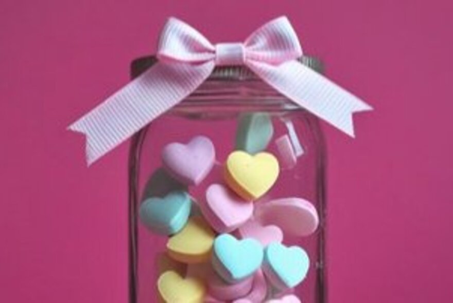 Jar filled with heart-shaped sweets tied with a bow.