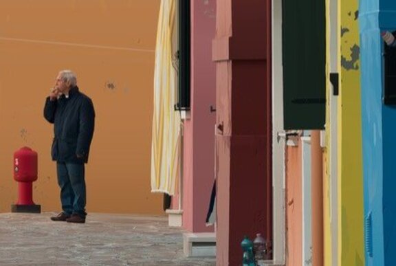 Digital image of a man smoking a cigarette in the distance, in a street with colourful buildings.