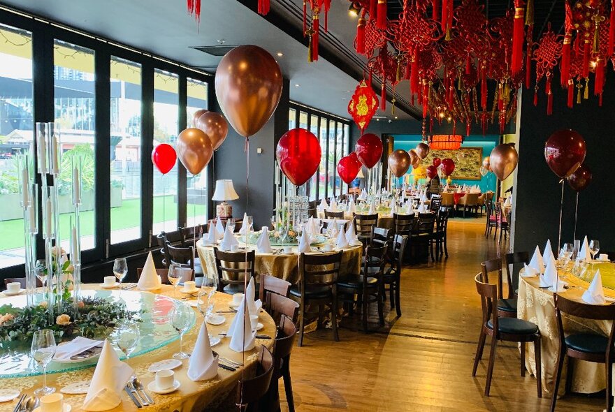 The interior of a restaurant's dining space decorated for an event with red and gold balloons.