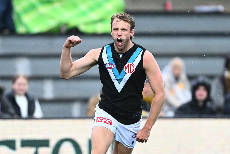 A Port Adelaide player fist pumps as he runs on the football field. 
