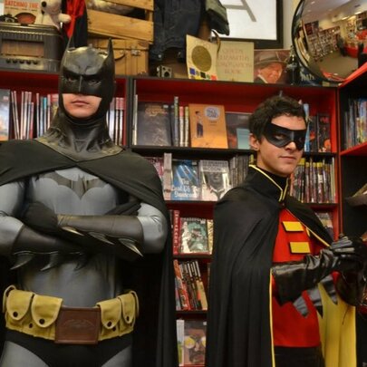 People dressed as Batman and Robin, standing in a comic store next to shelves of products.