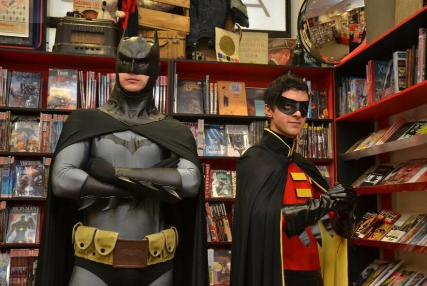 People dressed as Batman and Robin, standing in a comic store next to shelves of products.