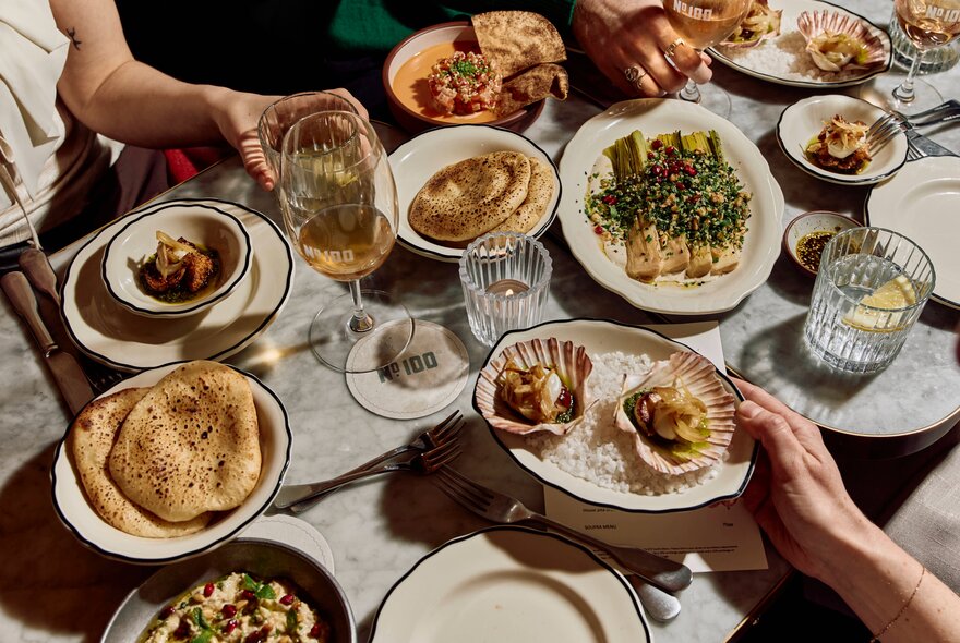 Looking down on a busy table set with many small plates and glasses of wine and water. 