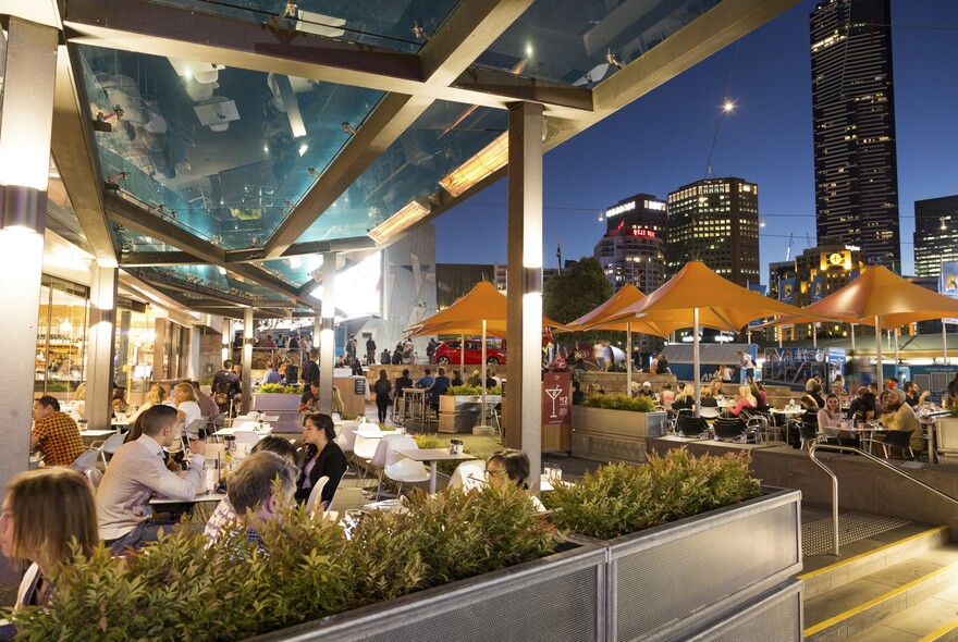 Patrons sitting outside under umbrellas at Time Out cafe in Fed Square at night.