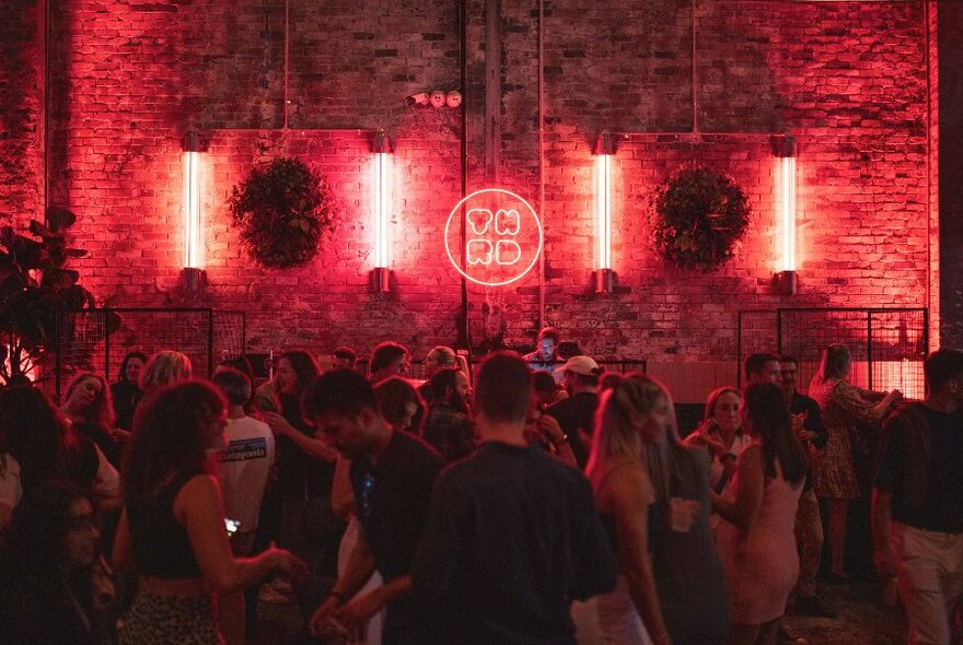 Neon lights illuminating a crowd of a people in a brick warehouse space.