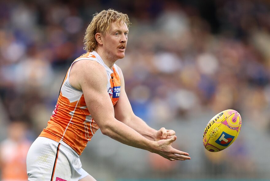 A GWS Giants AFL football player handballing  the yellow football during a match.