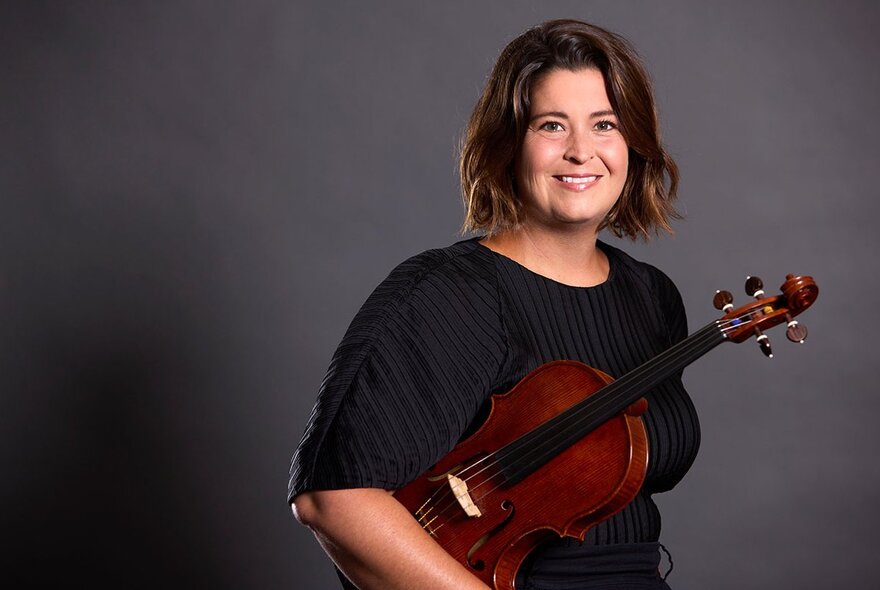 Female musician holding a violin under her arm and smiling.