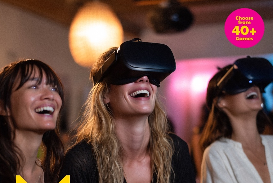 Three women, two with virtual reality headsets on, all laughing.