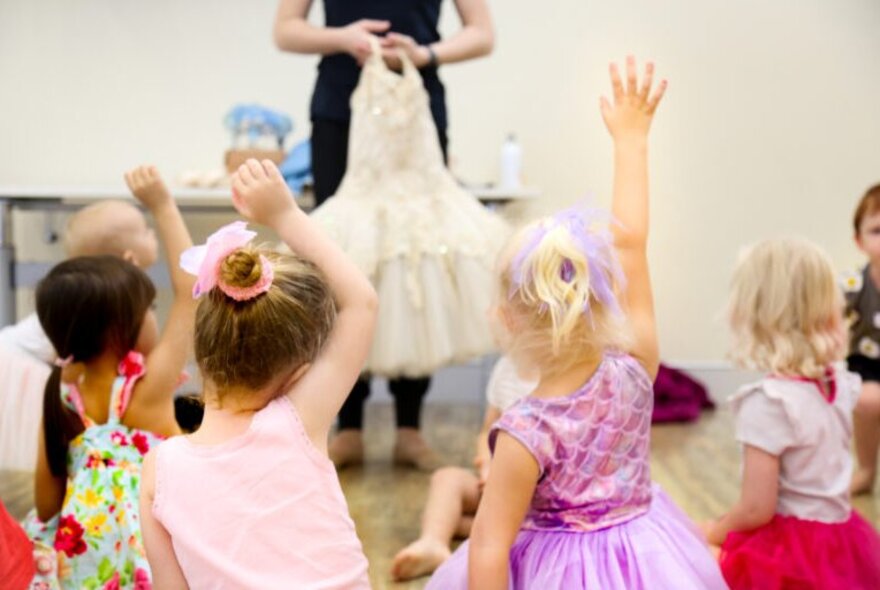 A group of young children dancing, all facing an instructor who stands at the front of the studio space.
