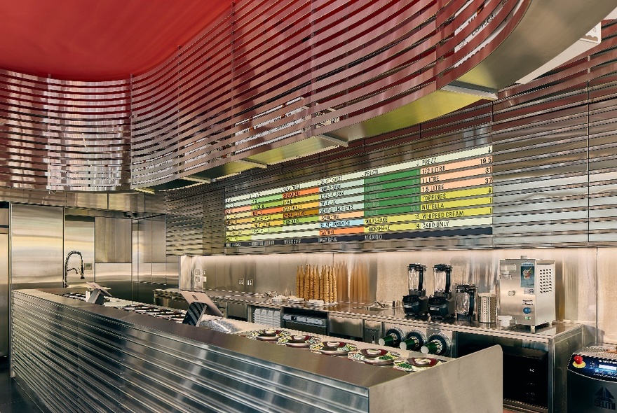 Interior of Piccolina gelato store with a curved silver counter, reflected in a curved stainless steel design suspended from the ceiling.