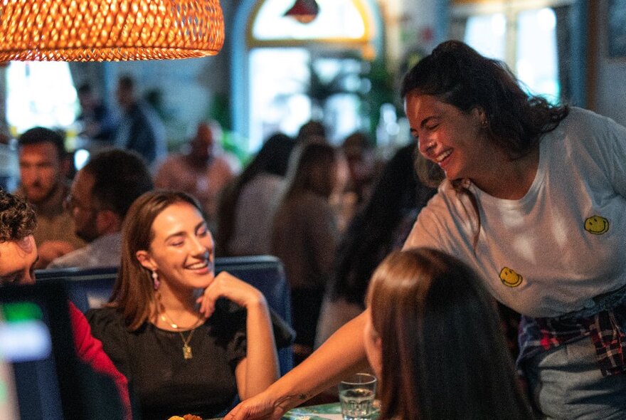 A waiter putting a dish on a table in front of two customers, in a busy cafe.