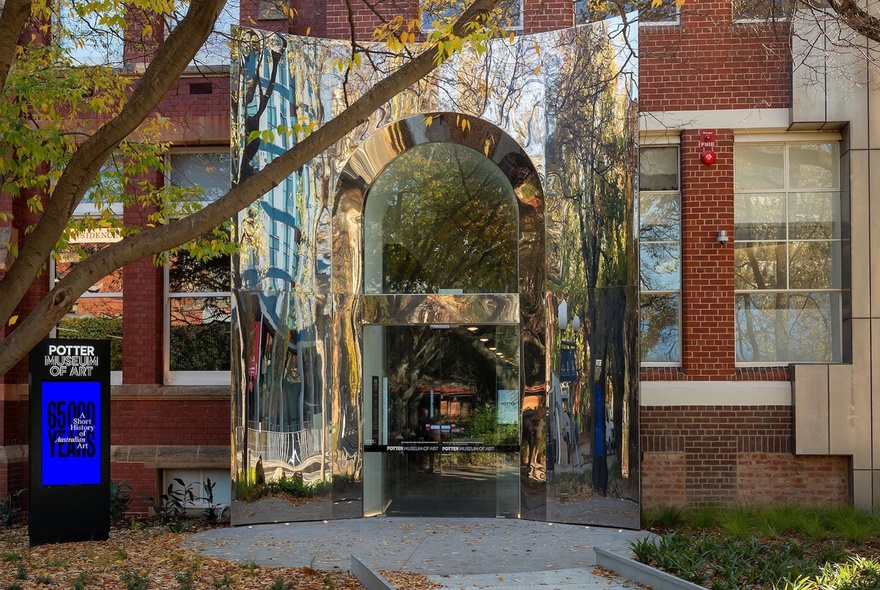 The reflective arched entrance to the Potter Museum of Art, a tree in the foreground.