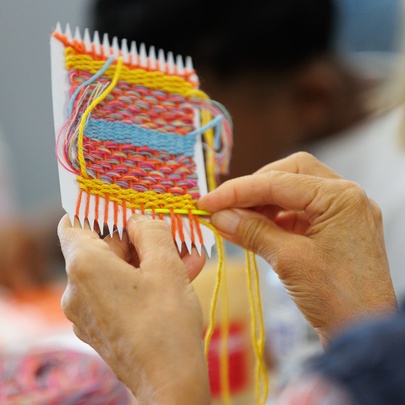 A close up over the shoulder image of someone weaving a small square. 