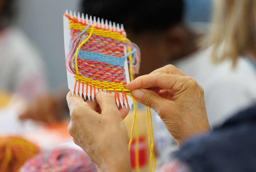 A close up over the shoulder image of someone weaving a small square. 