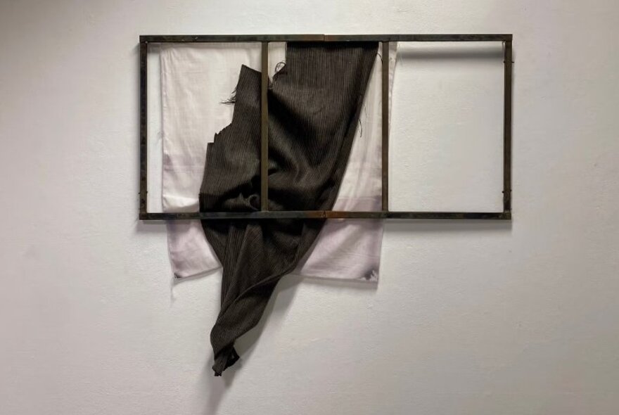 Artwork installation with ragged black and white cloth behind a window frame.