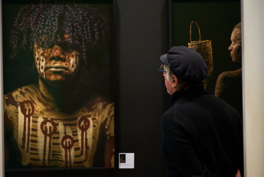 People viewing First Nations artwork showing a man with body paint. 