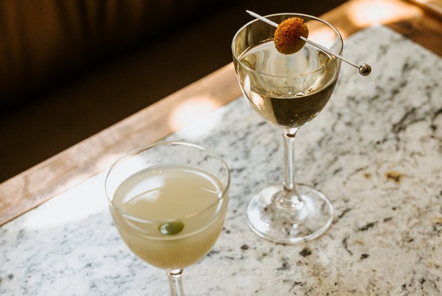 Two martinis served in small cocktail glasses on a marble table.